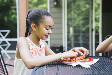 Smiling girl eating pizza in backyard on porch - MINF09419