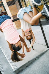 Happy, smiling girls hanging from bike rack bar on sidewalk - MINF09434