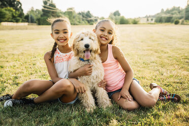 Porträt von lächelnden glücklichen Mädchen, die einen Labradoodle-Welpen im Park umarmen - MINF09438