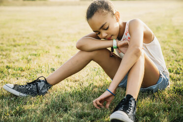 Girl sitting in field picking grass - MINF09439