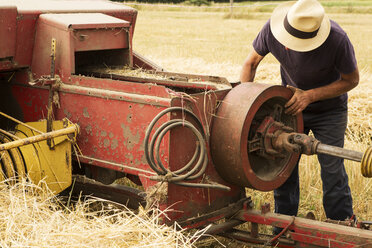 Traktor und Strohballenpresse in einem Weizenfeld, ein Landwirt überprüft seine Ausrüstung. - MINF09485
