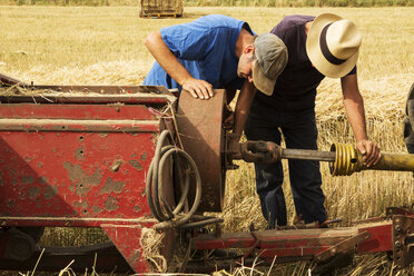 Traktor und Strohballenpresse in einem Weizenfeld, zwei Landwirte überprüfen die Ausrüstung. - MINF09487