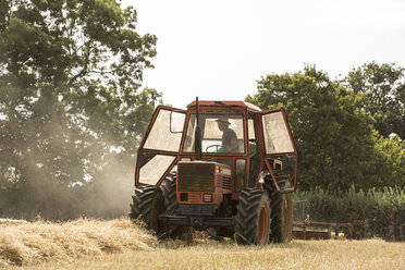 Traktor und Strohballenpresse in einem Weizenfeld, Landwirt presst Stroh. - MINF09490