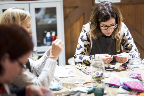 Eine Gruppe von Frauen, die in einer Werkstatt um einen Tisch sitzen und Stoffblumen herstellen. - MINF09498
