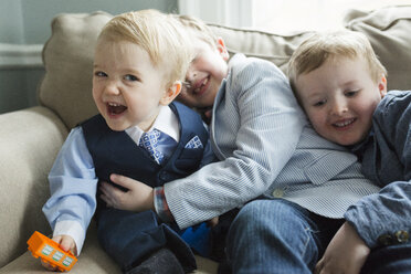 Fröhliche Brüder in Anzügen, die während des Osterfestes zu Hause auf dem Sofa sitzen - CAVF53175