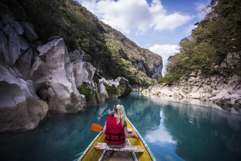 Rear view of woman sitting in boat on river amidst mountains against sky stock photo