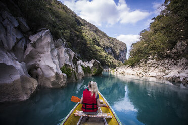 Rear view of woman sitting in boat on river amidst mountains against sky - CAVF53191