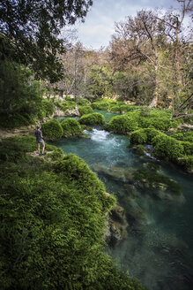 Rückansicht einer am Fluss stehenden Frau auf einer Wiese im Wald - CAVF53193