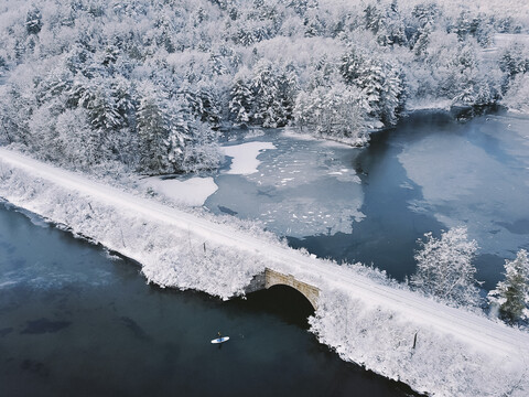 Hohe Winkel Ansicht der Person Paddleboarding im See von Brücke im Winter, lizenzfreies Stockfoto