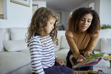 Mutter liest ihrer Tochter ein Bilderbuch vor, während sie zu Hause auf dem Sofa sitzt - CAVF53211