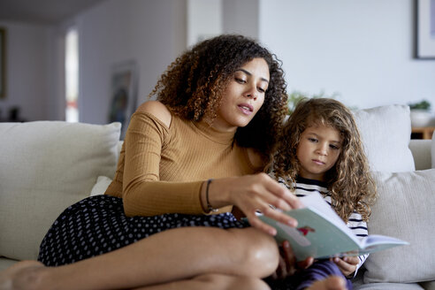 Niedriger Blickwinkel der Mutter lesen Bilderbuch für niedliche Tochter, während auf dem Sofa zu Hause sitzen - CAVF53215