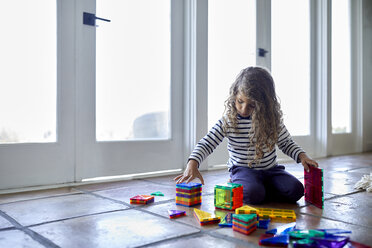 Cute girl playing with colorful toy blocks while kneeling on floor at home - CAVF53216