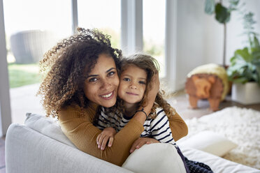 Porträt einer Mutter, die ihre Tochter umarmt, während sie zu Hause auf dem Sofa sitzt - CAVF53222