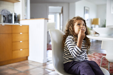 Girl looking away while eating food on chair at home - CAVF53233