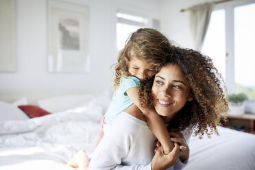 Happy daughter embracing mother sitting on bed at home - CAVF53240