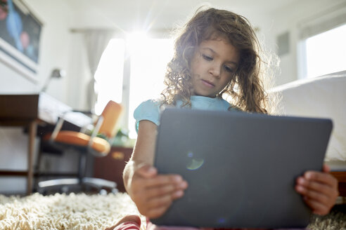 Low angle view of girl using tablet computer while kneeling on rug in bedroom - CAVF53245