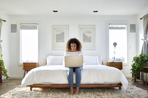 Frau benutzt einen Laptop, während sie zu Hause auf dem Bett sitzt - CAVF53255
