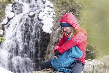 Lächelnde Frau mit Rucksack vor einem Wasserfall in den White Mountains im Winter - CAVF53259