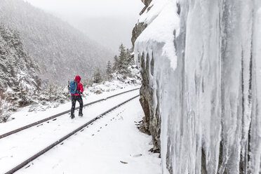 Rückansicht einer Frau, die bei Schneefall in den White Mountains auf einer verschneiten Bahnstrecke läuft - CAVF53260
