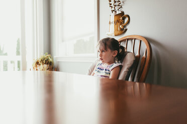 Thoughtful girl looking away while sitting on chair by wall at home - CAVF53272