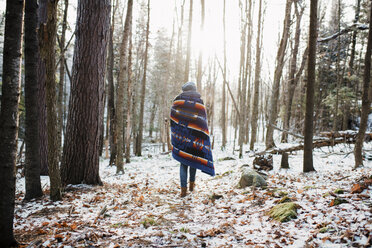Rückansicht einer Frau mit Decke, die im Winter im Algonquin Provincial Park im Wald spazieren geht - CAVF53280