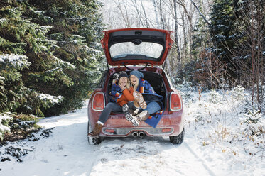 Fröhliche Freundinnen sitzen im Kofferraum eines Autos im Algonquin Provincial Park im Winter - CAVF53281