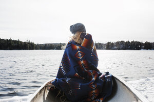 Rear view of woman with blanket sitting in boat on lake at Algonquin Provincial Park during winter - CAVF53288