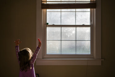 Mädchen mit erhobenen Armen am Fenster stehend zu Hause - CAVF53289