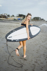 Fröhliche Frau mit Surfbrett beim Spaziergang am Strand - CAVF53306