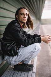 Portrait of man crouching on bench by wall - CAVF53312