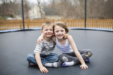 Porträt eines glücklichen Geschwisterpaares auf einem Trampolin auf einem Spielplatz - CAVF53318