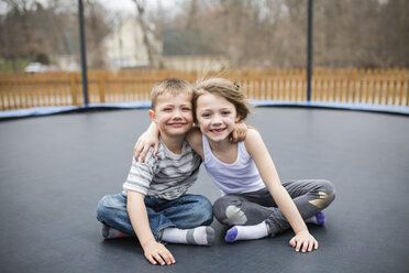 Portrait of happy siblings sitting on trampoline at playground - CAVF53318