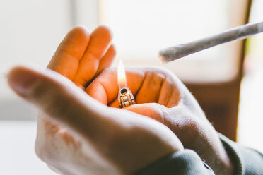 Abgeschnittene Hände eines Mannes, der zu Hause einen Marihuana-Joint mit einem Feuerzeug anzündet - CAVF53328