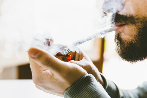 Mittelteil eines bärtigen Mannes, der zu Hause einen Marihuana-Joint raucht, lizenzfreies Stockfoto