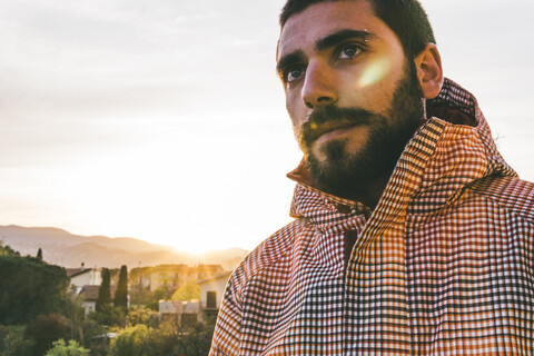 Nachdenklicher junger Mann mit Kapuzenhemd, der bei Sonnenuntergang in den Himmel schaut, lizenzfreies Stockfoto