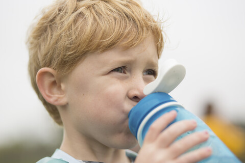 Nahaufnahme eines Jungen, der beim Trinken von Wasser vor dem Himmel wegschaut, lizenzfreies Stockfoto