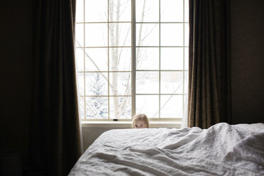 Portrait of girl hiding behind bed at home - CAVF53345