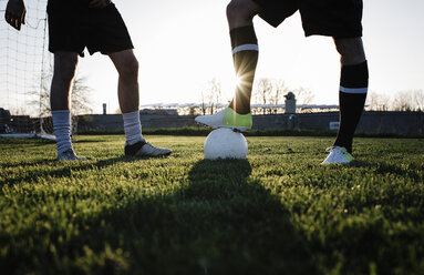 Low section of male friends playing soccer on grassy field against clear sky at park - CAVF53360