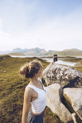 Norwegen, Lofoten, junge Frau macht Selfie mit Smartphone in der Natur - RSGF00055