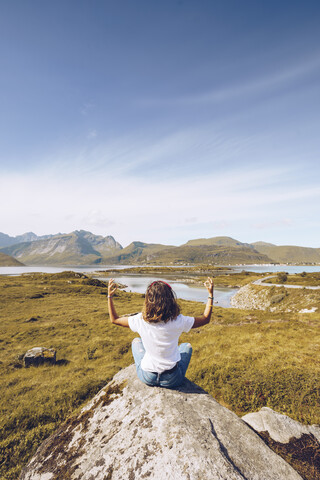 Norway, Lofoten, back view of young woman sitting on a rock doing yoga stock photo