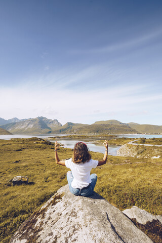 Norwegen, Lofoten, Rückenansicht einer jungen Frau, die auf einem Felsen sitzt und Yoga macht, lizenzfreies Stockfoto
