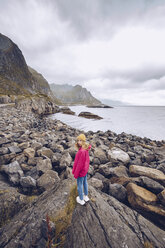 Norwegen, Lofoten, junge Frau in Regenjacke auf einem Felsen stehend - RSGF00065