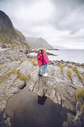 Norwegen, Lofoten, zwei Frauen in Regenjacken stehen Rücken an Rücken auf einem Felsen - RSGF00066