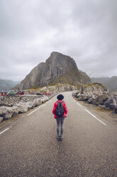 Norwegen, Lofoten, Hamnoy, Rückenansicht eines Mannes mit Rucksack, der auf einer leeren Straße steht - RSGF00067