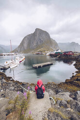 Norway, Lofoten, Hamnoy, back view of man wearing red rainjacket and backpack looking at view - RSGF00069