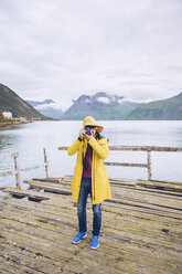 Norwegen, Senja, Mann steht auf einem baufälligen Steg an der Küste und macht ein Foto - RSGF00078