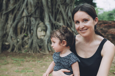 Thailand, Ayutthaya, portrait of smiling mother and daughter visiting the Buddha head in between tree roots at Wat Mahathat - GEMF02464