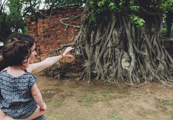 Thailand, Ayutthaya, Mutter und Tochter beim Fotografieren des Buddha-Kopfes zwischen Baumwurzeln im Wat Mahathat - GEMF02465