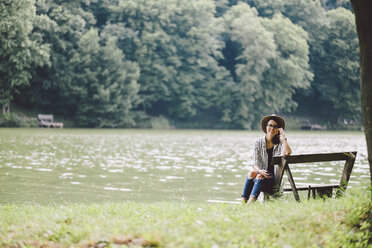 Porträt einer Frau, die auf einer Bank am Seeufer im Wald sitzt - CAVF53399