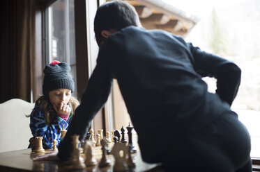 Geschwister spielen Schach, während sie zu Hause am Fenster stehen - CAVF53413